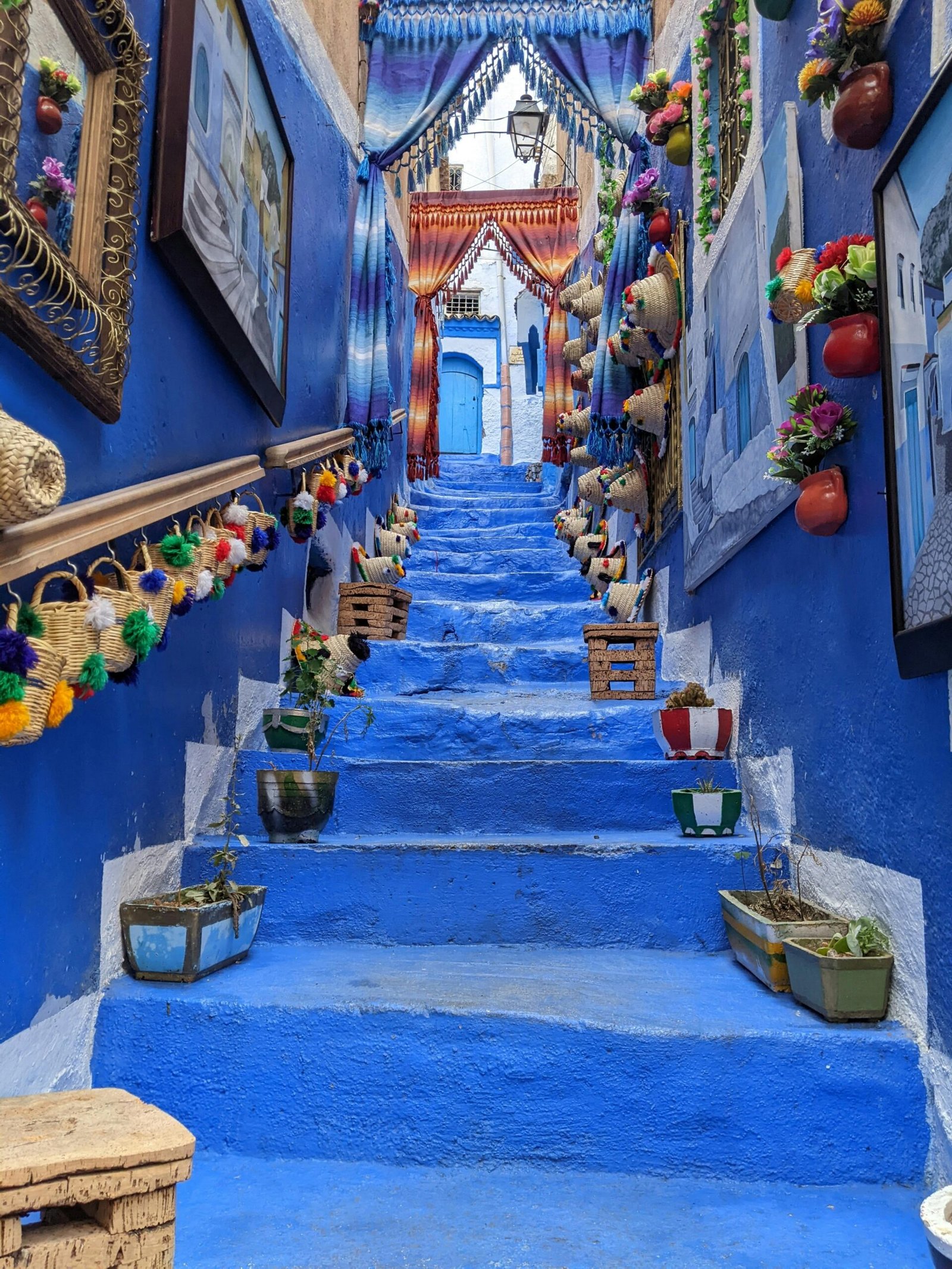 A cobalt-blue stairway lined with woven baskets and textiles in Chefchaouen